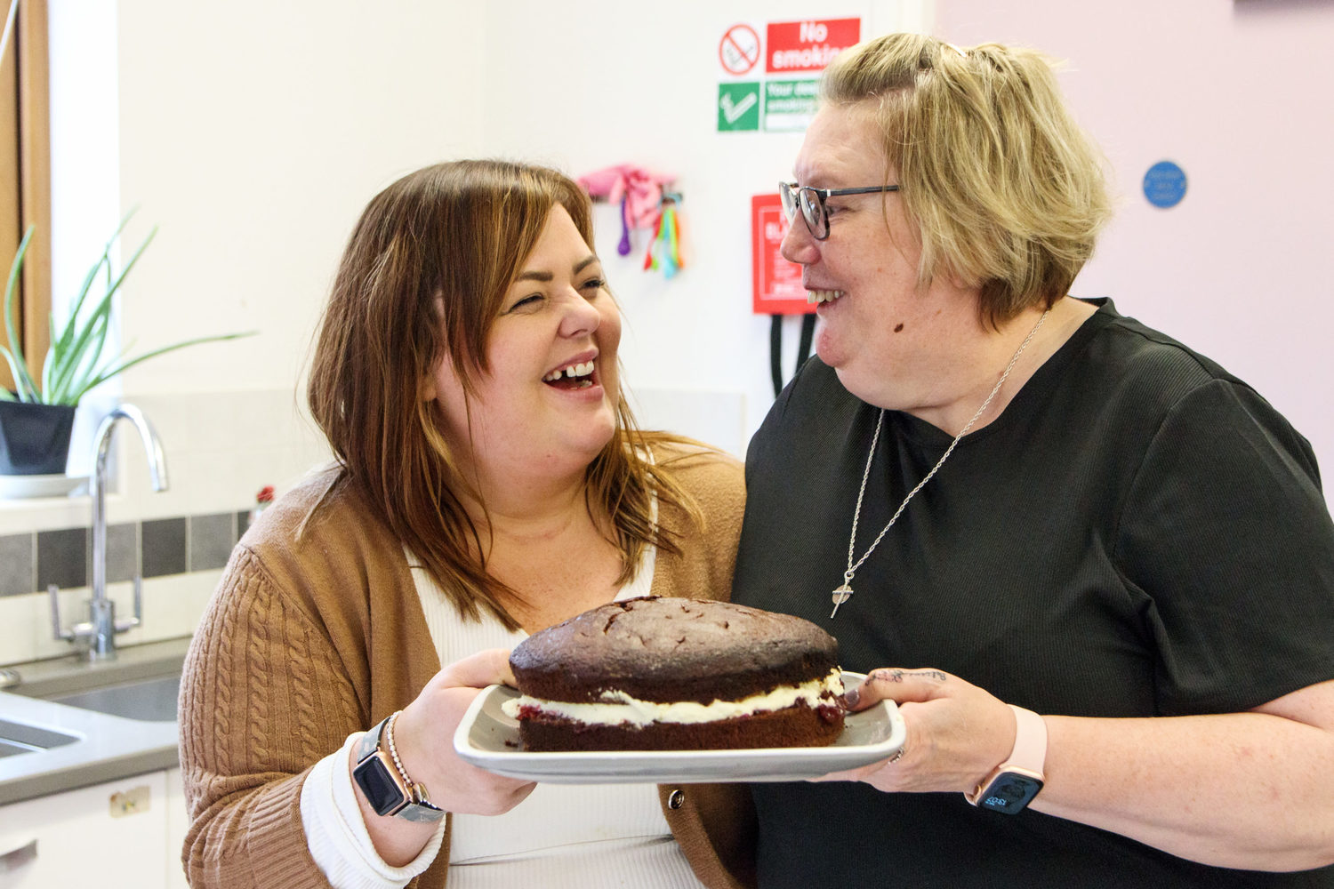 Two ladies, holding a chocolate cake, smiling and laughing