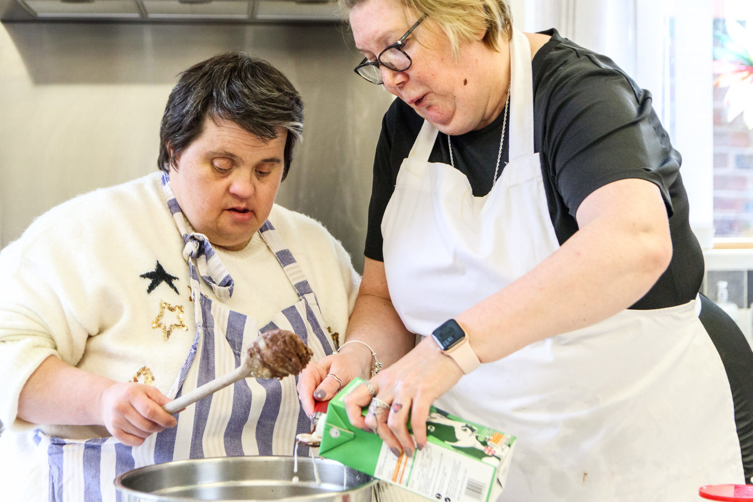 “What matters most is offering friendship and kindness. Connecting with other people and being happy,” says Michelle. Two ladies putting chocolate icing into a piping bag to bake a cake