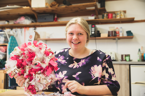 Girl called Chloe holding up a rag wreath she has made in the art studio