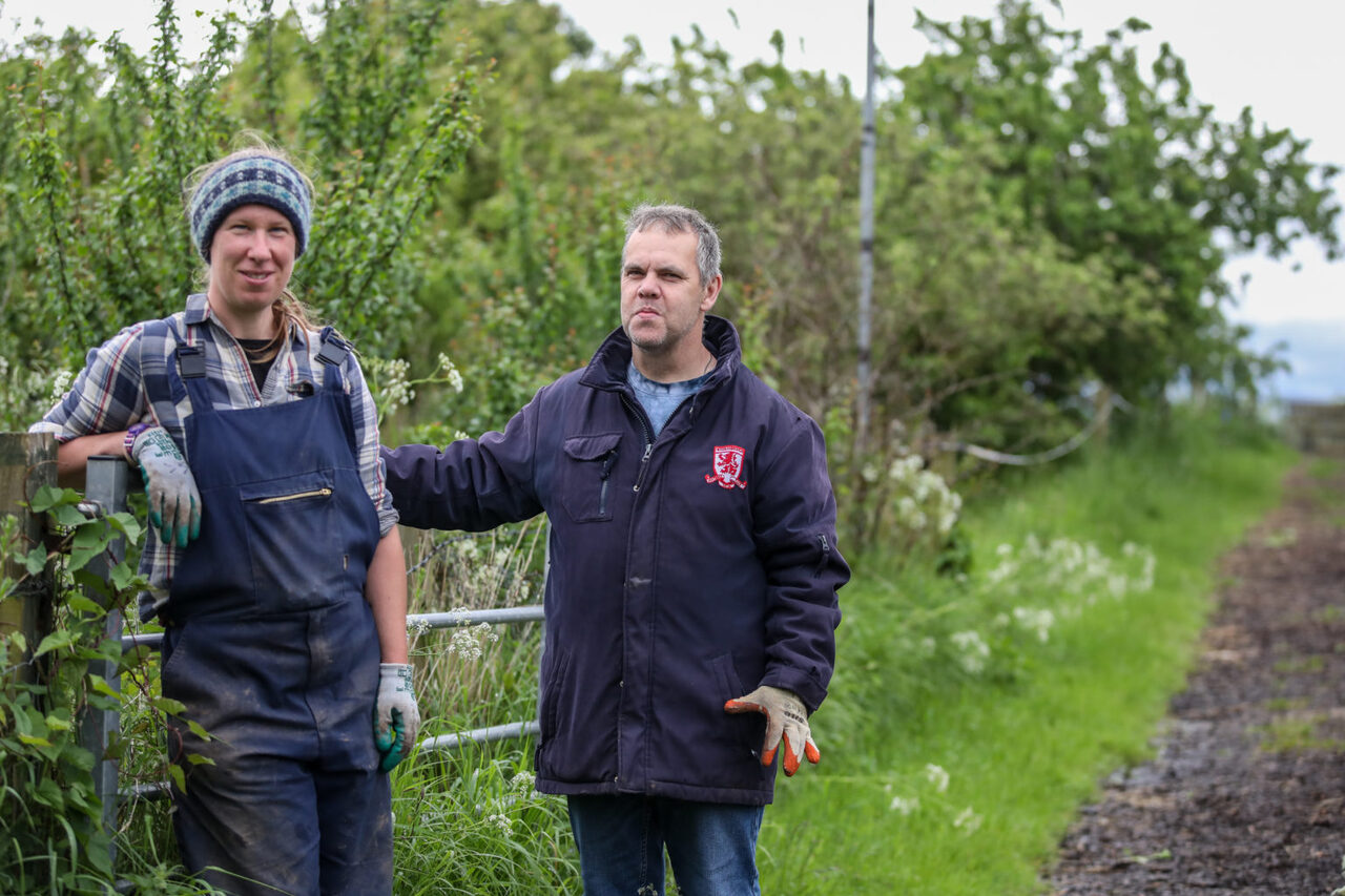 A support worker and person we support leaning on a gate smiling outside