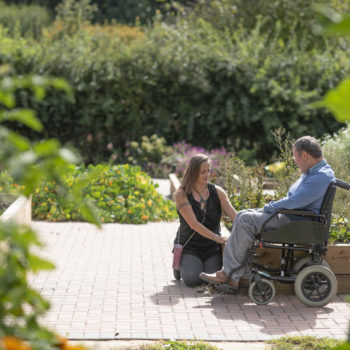 A person we support in a wheelchair with a support worker sitting outside in the garden