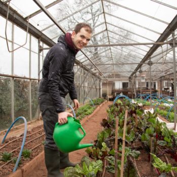 A person support in one of our green houses watering the plants and smiling