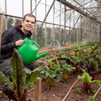 A person we support watering plants in a greenhouse and smiling