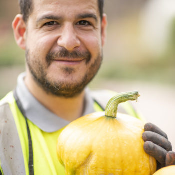 A person we support smiling and holding homegrown orange pumpkins