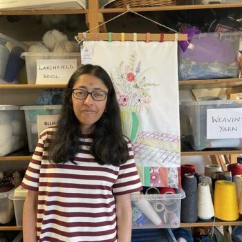 A person standing next to a stitched artwork