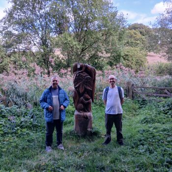 Two people standing next to a totem pole