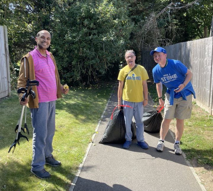 3 men with litter pickers and rubbish bags cleaning an alleyway, they are smiling and pulling faces at the camera