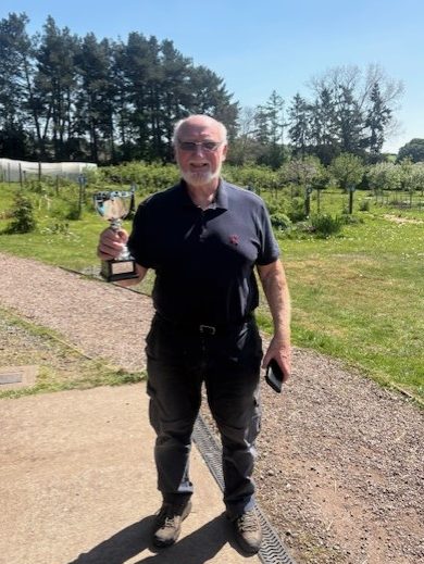 A man standing in front of a garden backdrop holding a trophy