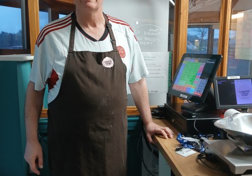 A man in a Camphill Village Trust apron behind a till