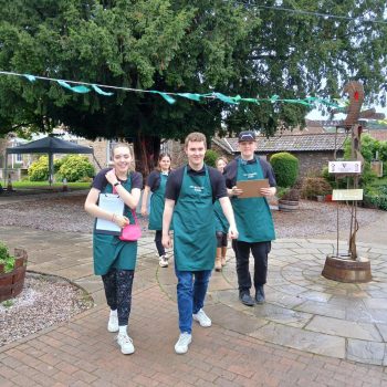 A group of trainees at Severnside skills, they are wearing green aprons and walking towards the camera smiling.