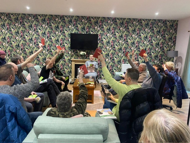 Group taking part in cancer prevention session, they are holding up red cards in a bold, patterned room.