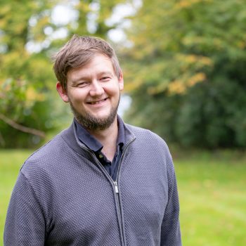Photo of Alex Digby, he is standing outside, smiling at the camera.