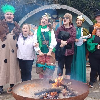 People wearing fancy dress standing around a wood fire