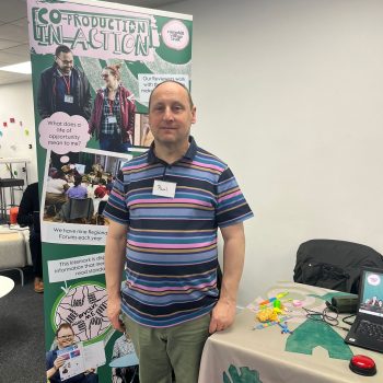 Paul smiling next to a banner