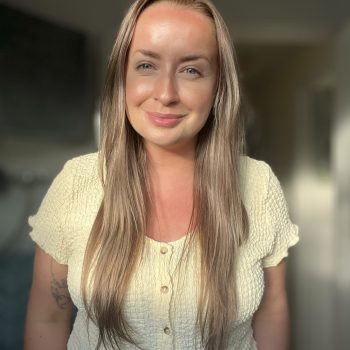 Headshot of Emma smiling at the camera in a sun-dappled room