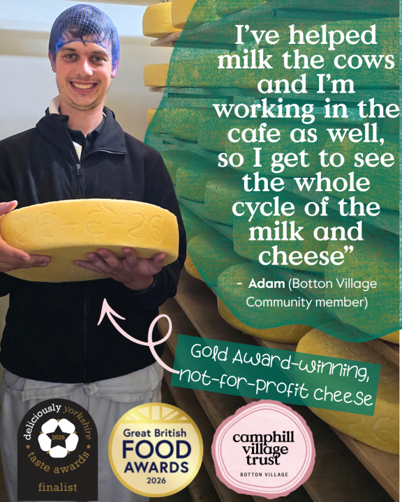 Community member Adam holding a wheel of award-winning Summerfields cheese in the Botton Village creamery, reflecting the journey from caring for the dairy herd to producing artisan cheese sold in the café and at local markets.
