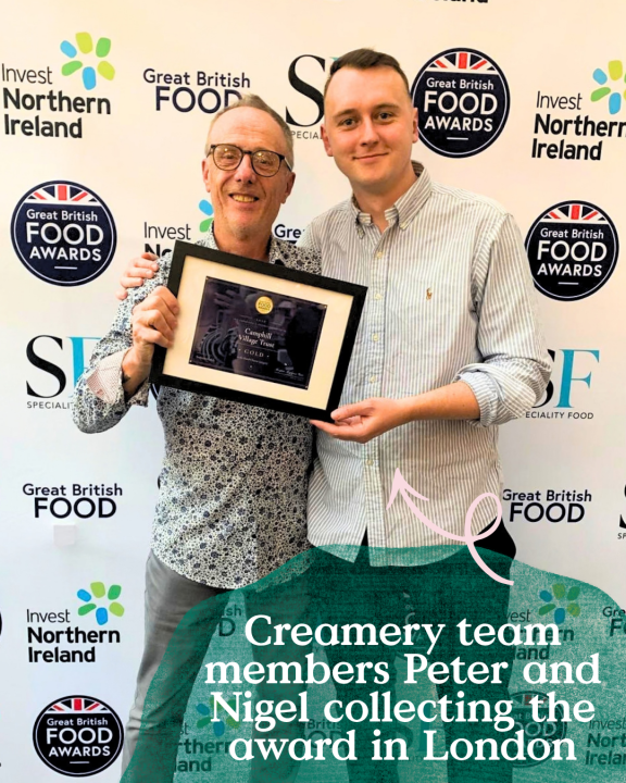 Two representatives from Camphill Village Trust holding a Gold Award certificate at the Great British Food Awards, celebrating Summerfields cheese's award-winning success in front of the event backdrop.